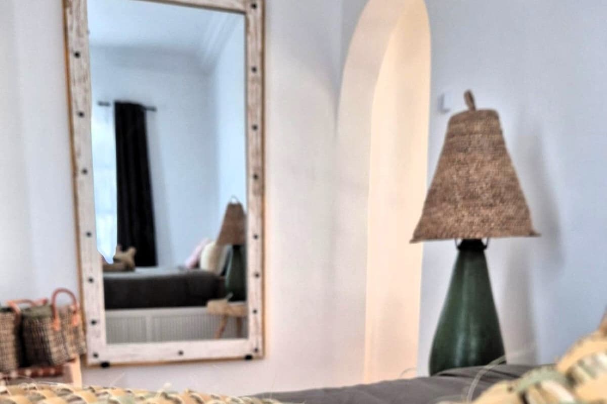 Quarto com cabeceira de tecido, espelho, abajur e cama.