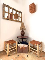 Habitación de esquina con un espejo de madera rústica, una lámpara tejida, dos sillas tejidas, una mesita redonda y una cesta tejida.