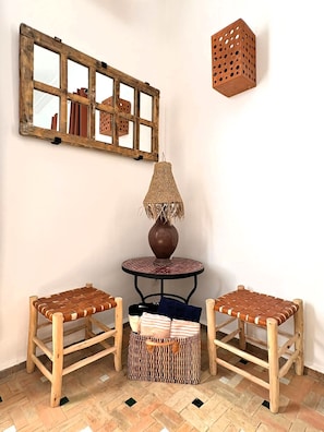A corner room with a rustic wooden mirror, a woven lamp, two woven chairs, a small round table, and a woven basket. - Villa Dar Serenity (Ounagha)