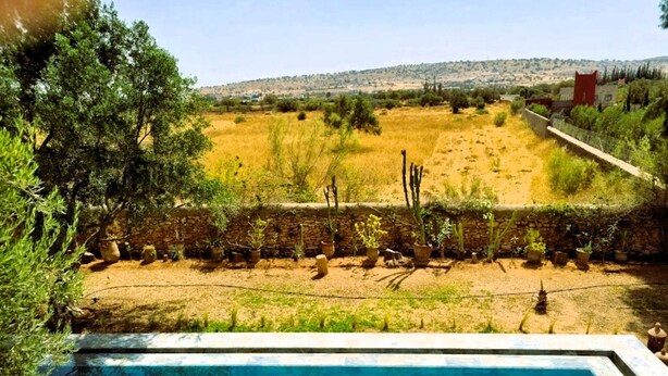 A swimming pool with a view of a dry, grassy area and a distant hill. - Villa Dar Serenity (Ounara)