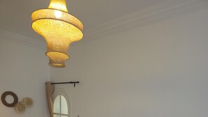 A bedroom with a large bed, a bedside table with a lamp, a hanging light fixture, and a window with curtains. - Villa Dar Serenity (Ounara)
