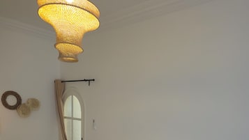 A bedroom with a large bed, a bedside table with a lamp, a hanging light fixture, and a window with curtains.