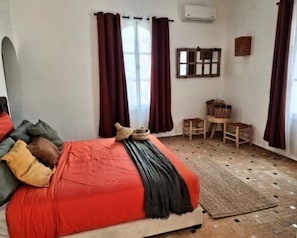 Un dormitori amb un llit, una finestra amb cortines, una taula petita i una cadira.