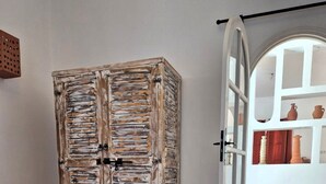 A room with a rustic wooden wardrobe, a bed with a green blanket, and a wicker basket. - Villa Dar Serenity (Ounara)