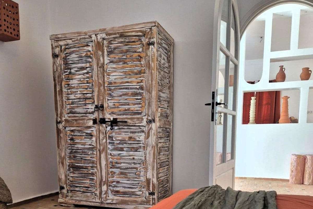 Quarto com guarda-roupa de madeira rústica, cama com manta verde e cesto de vime.