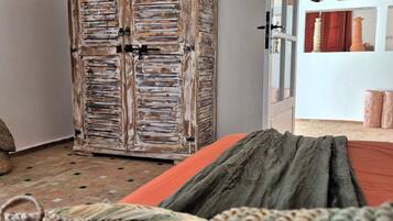 Een kamer met een rustieke houten garderobe, een bed met een groene deken en een rieten mand.