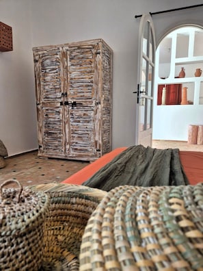 Quarto com guarda-roupa de madeira rústica, cama com manta verde e cesto de vime.