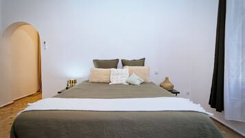 A bedroom with a bed, pillows, a bedside table, a lamp, and a wall-mounted switch.