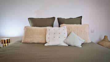 Una cama con una manta color beige y varias almohadas de distintas texturas y colores.
