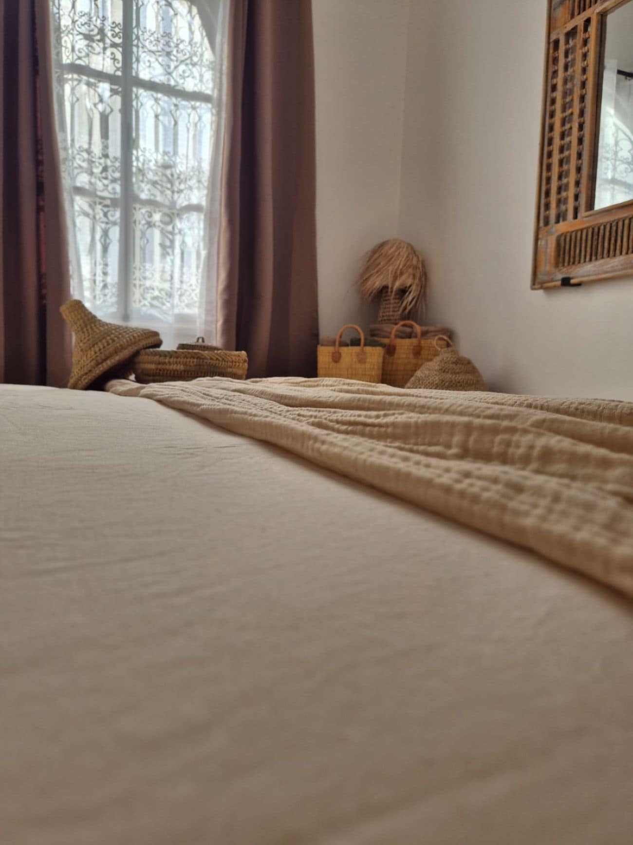 Un dormitorio con cama, ventana con cortinas y espejo en la pared.