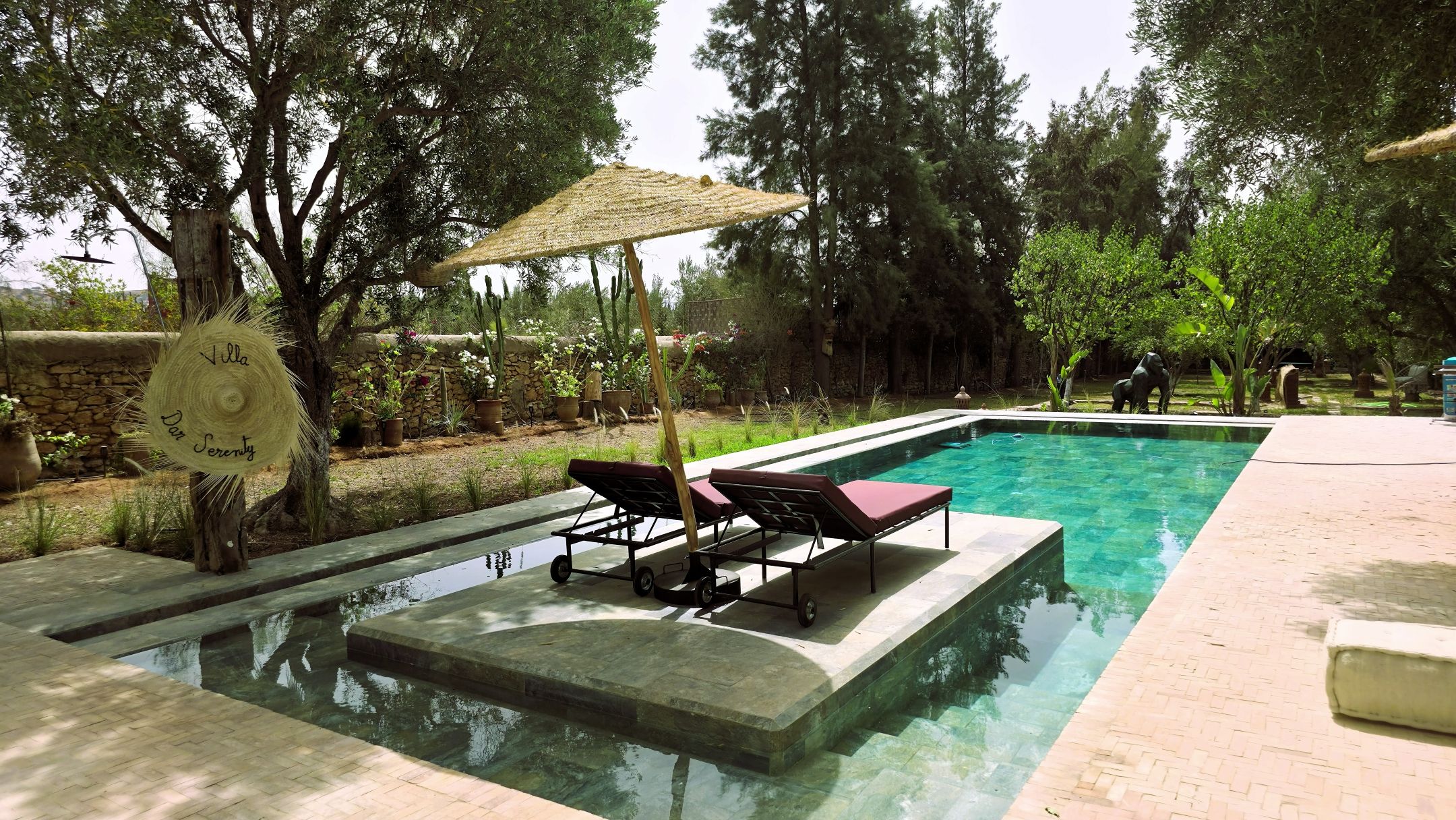 Una piscina con sillones de descanso, una pérgola y un muro de piedra.