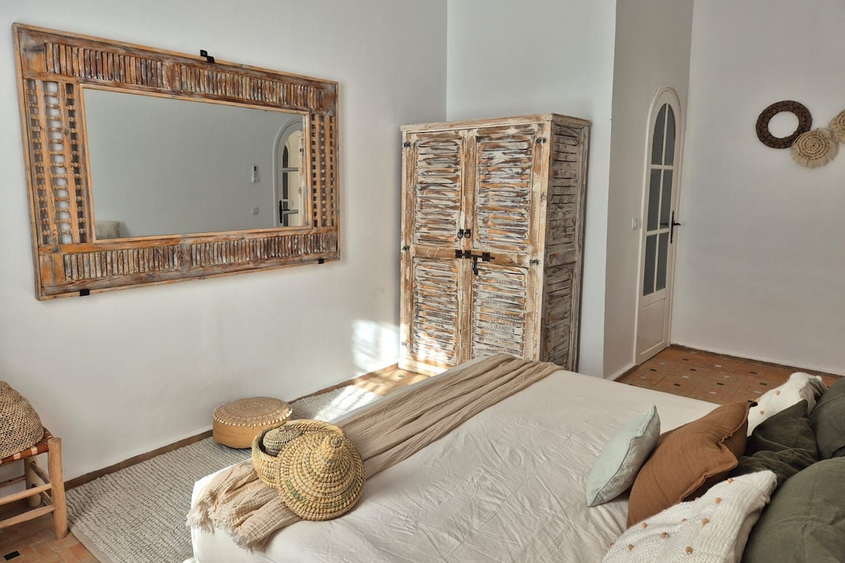 A bedroom with a large mirror, a wardrobe, a bed with a woven basket, and a small seating area.