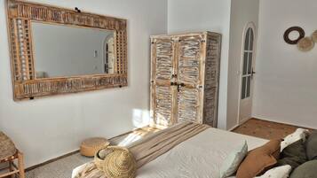 Un dormitorio con un espejo grande, un armario, una cama con una cesta tejida y una pequeña zona de estar.