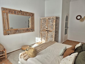 A bedroom with a large mirror, a wardrobe, a bed with a woven basket, and a small seating area. - Villa Dar Serenity (Ounagha)