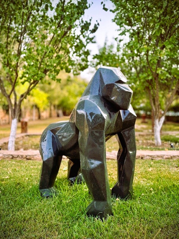 A sculpture of an animal in a park with grass and trees.