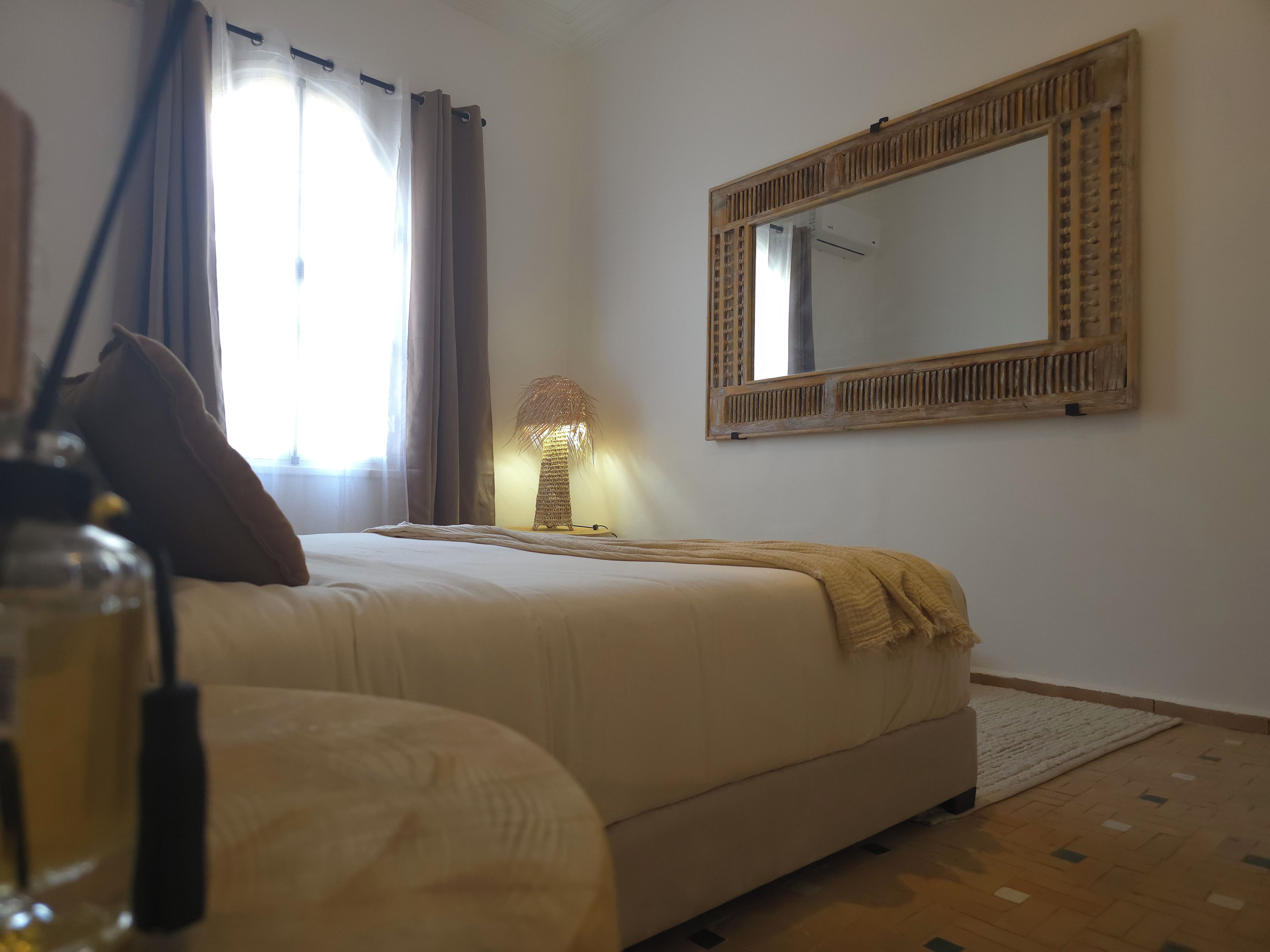Een slaapkamer met een bed, een bedlampje, een spiegel en een raam met gordijnen.