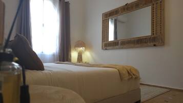 Een slaapkamer met een bed, een bedlampje, een spiegel en een raam met gordijnen.