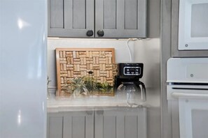 A kitchen with grey cabinets, a coffee maker, and a decorative corkboard. - Lake Michigan Cottage - Sleeps 14 - Private Beach + Sunset Views (Harbor Springs)
