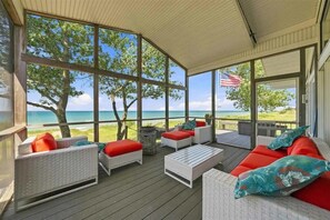 A covered outdoor seating area with wicker furniture and red cushions, overlooking a beach and ocean.