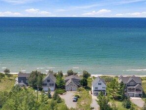A coastal residential area with houses near the beach, a clear sky, and a view of the ocean. - Lake Michigan Cottage - Sleeps 14 - Private Beach + Sunset Views (Harbor Springs)