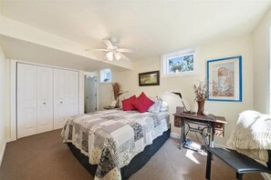 A bedroom with a bed, a desk, a chair, a bench, a ceiling fan, and a wardrobe.