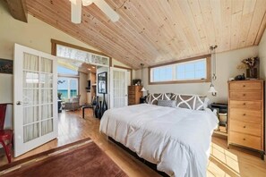 A bedroom with a large bed, wooden ceiling, and a view of the outdoors.