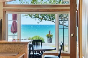 A dining area with a view of the ocean, a wooden table, chairs, and a potted plant.