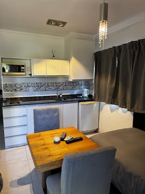 A compact kitchenette with a microwave, a kettle, and a small refrigerator. There is a dining table with a chair and a remote control on it. - Hotel Dinastie Palace  (Chajarí)