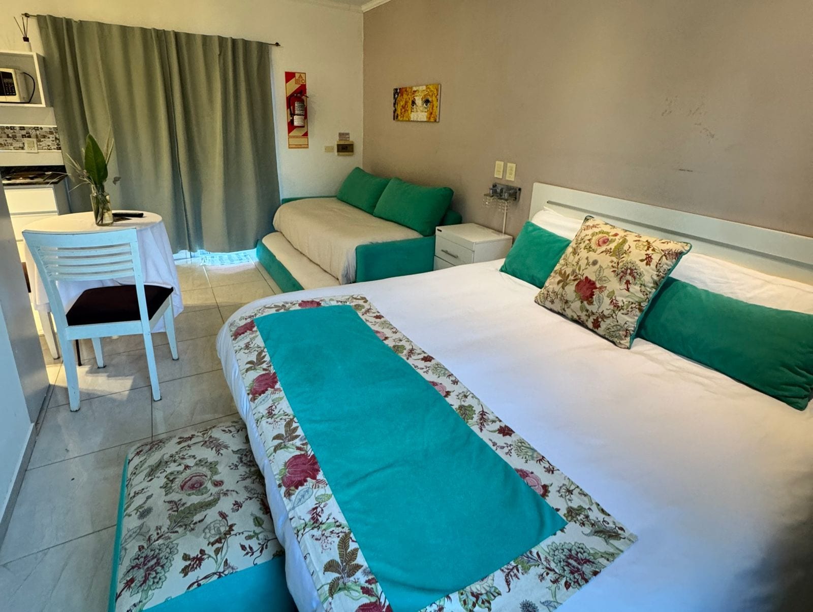Quarto de hotel com cama, cadeira, mesa de cabeceira, telefone fixado na parede e janela com cortinas.