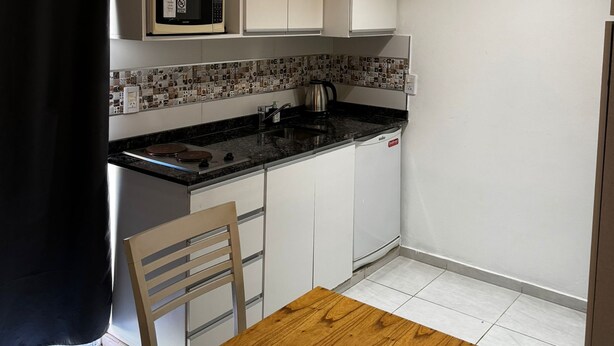 A compact kitchen with white cabinets, a microwave, a kettle, and a wooden dining table.
