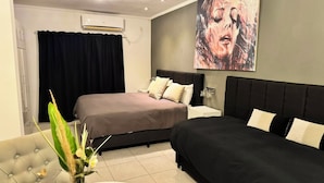 A hotel room with two beds, a dining table, a vase with flowers, and a large painting on the wall.