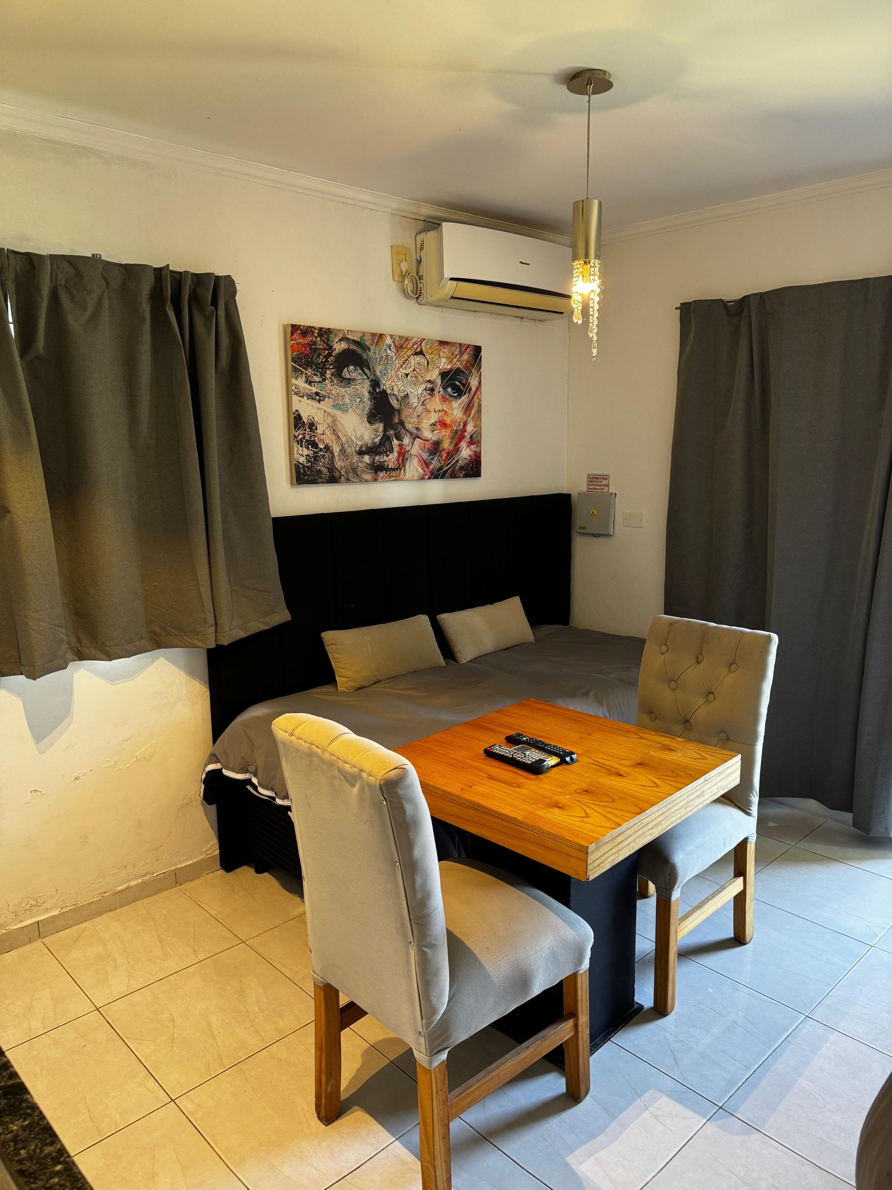 Una habitación con una cama, un cuadro, una mesa con sillas y un equipo de aire acondicionado.