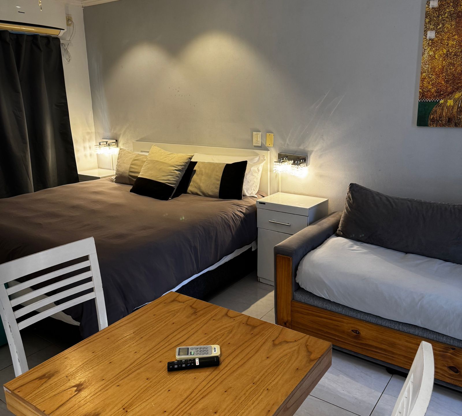 A hotel room with a bed, bedside tables, a sofa, a wooden table, and a chair.