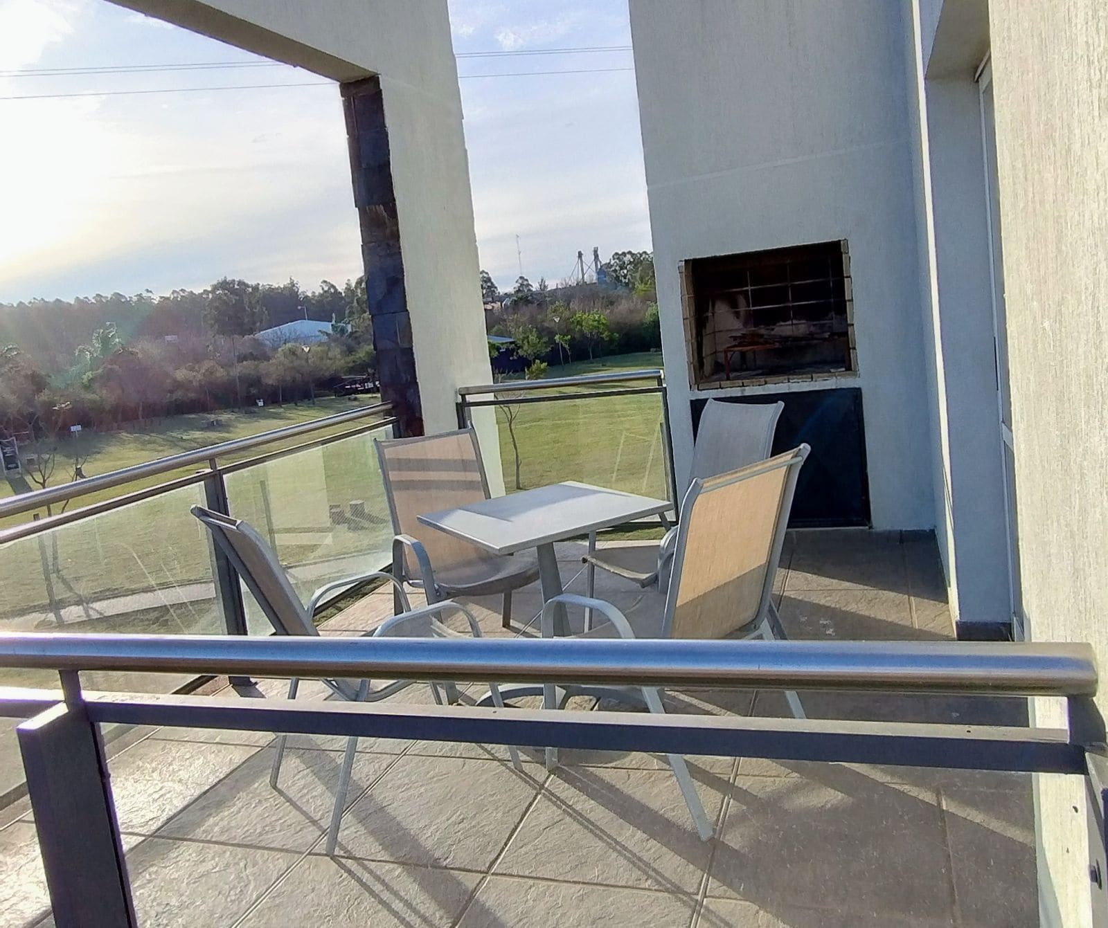 A balcony with a table and chairs, a grill, and a view of the surrounding area.