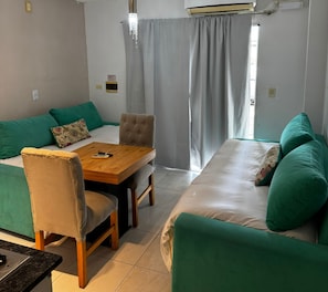 A room with a sofa, a dining table, and a chair. There is a window with curtains. - Hotel Dinastie Palace  (Chajarí)