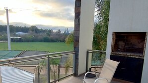 A balcony with a table and chairs, a grill, and a view of a green field.