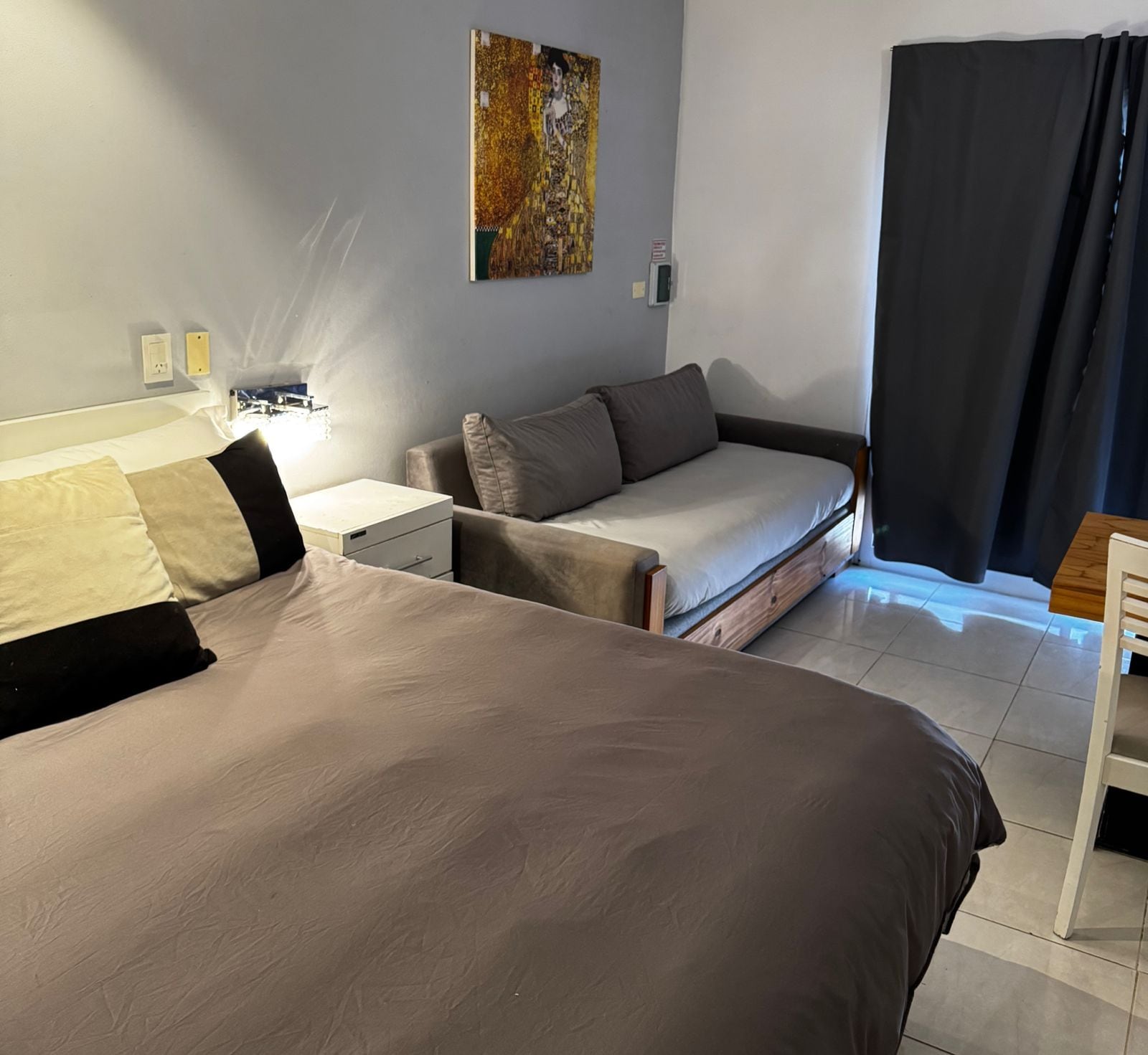 Un dormitorio con una cama grande, un sofá cama, una mesita de noche y un cuadro en la pared.