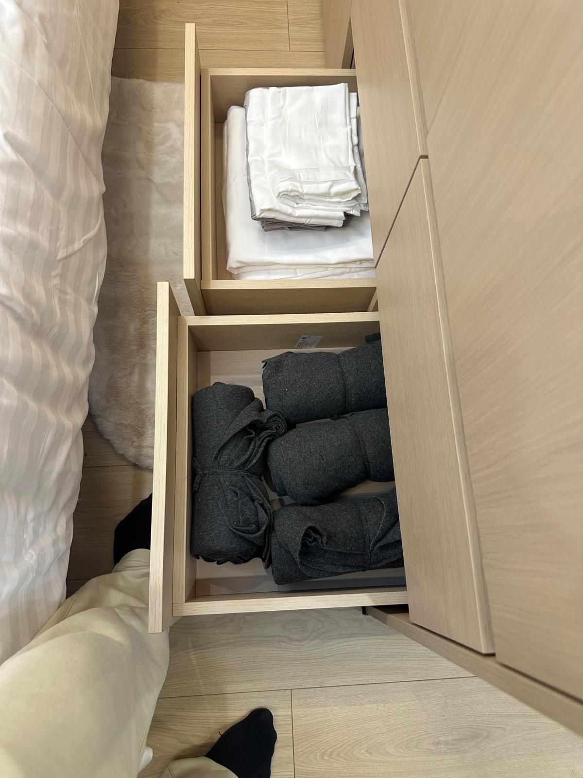 A bedroom with a bed, a wooden wardrobe, and a storage unit with folded clothes.