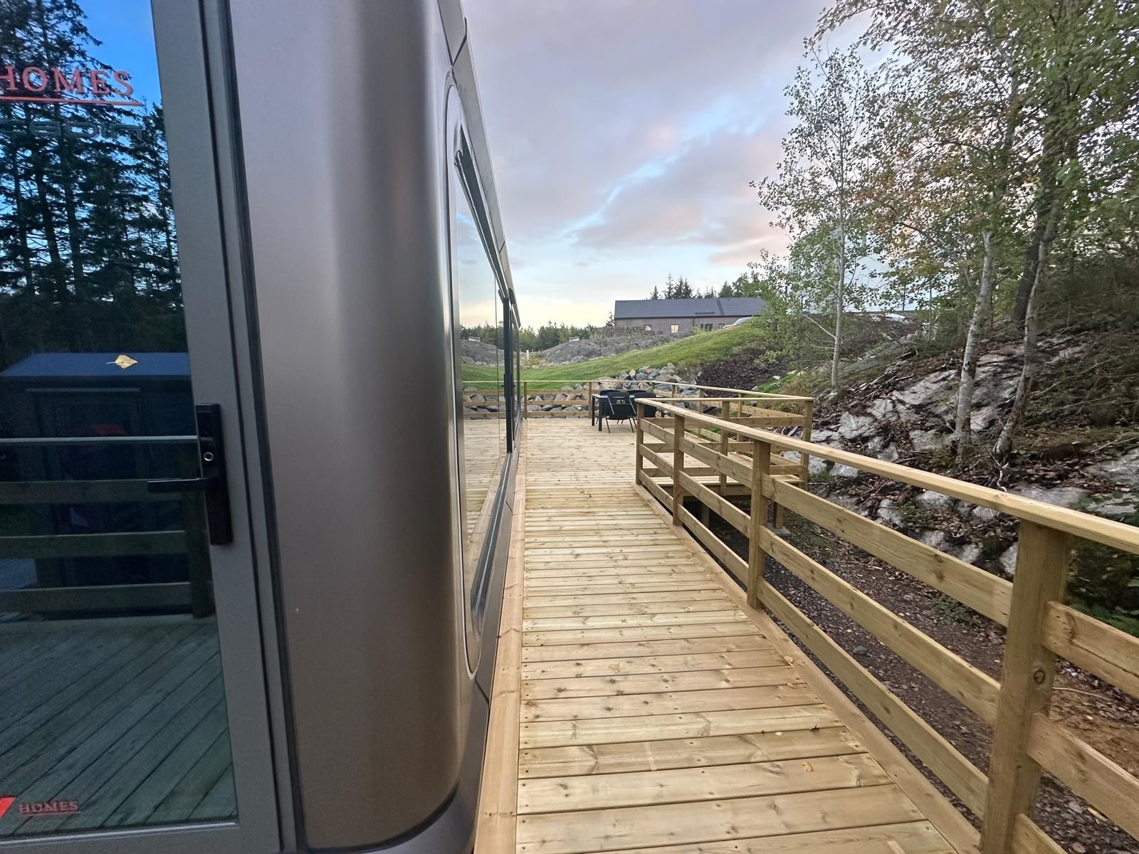 Ett trädäck som leder fram till en byggnad med utsikt över en kulle och träd.