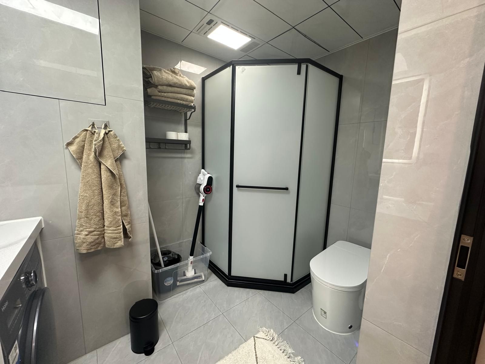 Une salle de bain moderne avec une douche d’angle, des toilettes, un lavabo et un porte-serviettes.