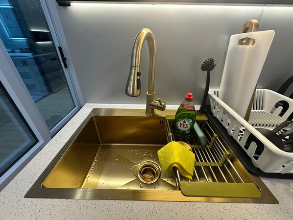 A kitchen sink with a gold faucet, a yellow sponge, and a dish rack with white dishes.