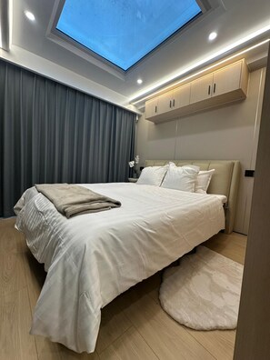 A modern bedroom with a skylight, a bed with white bedding, a nightstand, and a wardrobe.