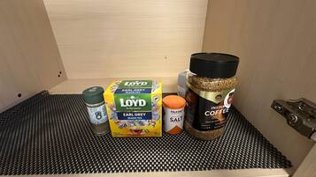 A drawer with a black mesh mat, containing a box of Earl Grey black tea, a salt container, and a jar of instant coffee.