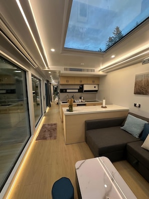 A modern interior with a kitchen, dining area, and seating space, featuring a skylight and wooden flooring. - 39-square-meter capsule house (Billdal)