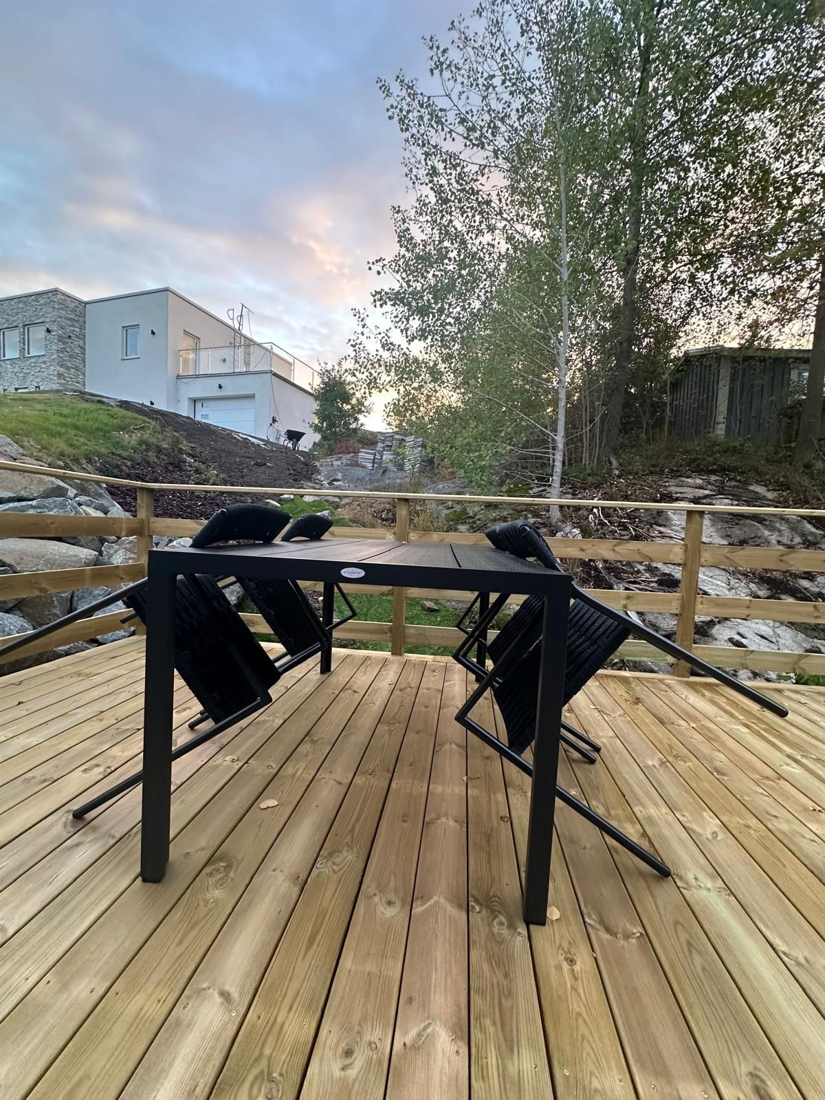 An outdoor deck with a table and chairs, surrounded by a wooden fence and trees.
