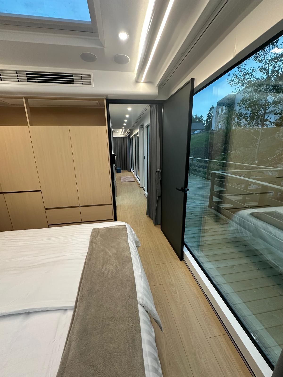 A modern bedroom with a large bed, built-in wardrobe, and a sliding glass door leading to a balcony.