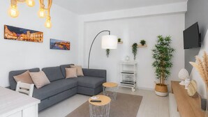 A modern living room with a grey sectional sofa, a coffee table, a side table, a floor lamp, a TV, and a bookshelf. - Villa Latina with Private Veranda, Wi-Fi, and Air Conditioning (Solarino)