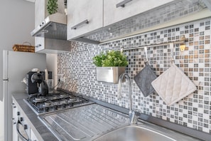 Eine moderne Küche mit Gasherd, Edelstahlspüle und einer Spritzschutzwand mit Mosaikfliesenmuster.