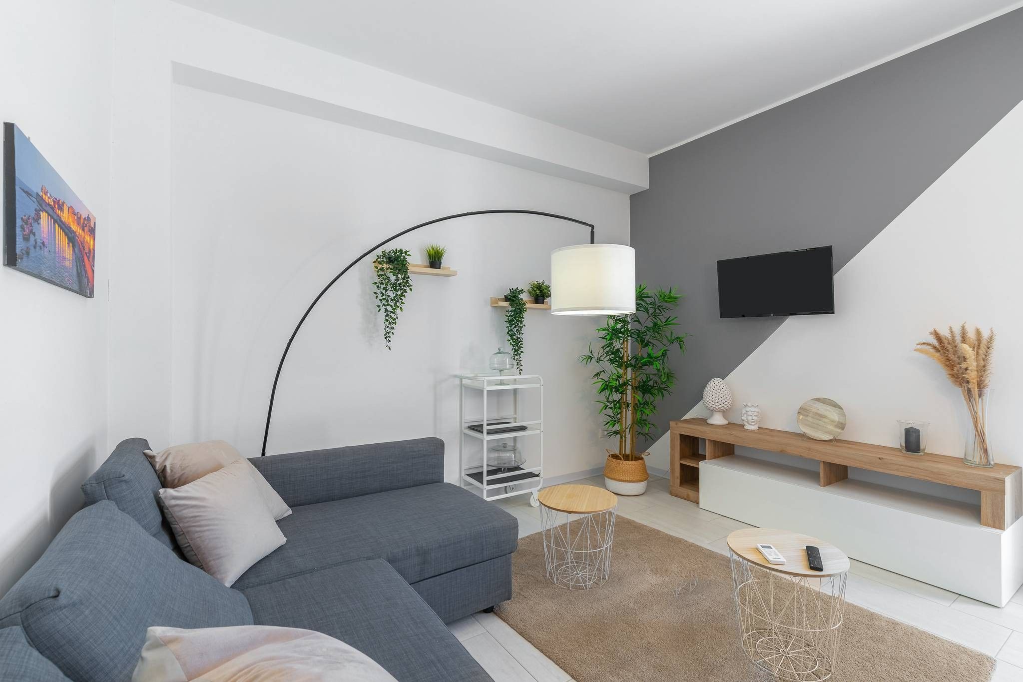Ein modernes Wohnzimmer mit einem grauen Sofa, einer weißen Unterhaltungseinheit, einer Stehlampe und einem an der Wand befestigten Fernseher.