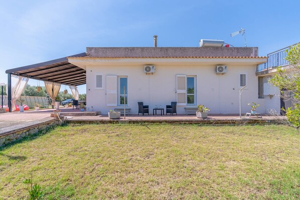 A two-story building with a covered patio area, outdoor seating, and a grassy yard.